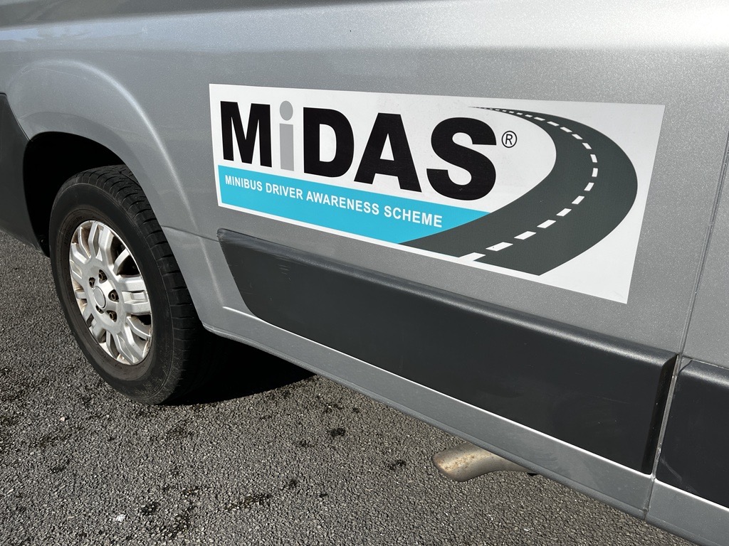 grey minibus side and wheel arch with a black, white and blue MiDAS logo sticker