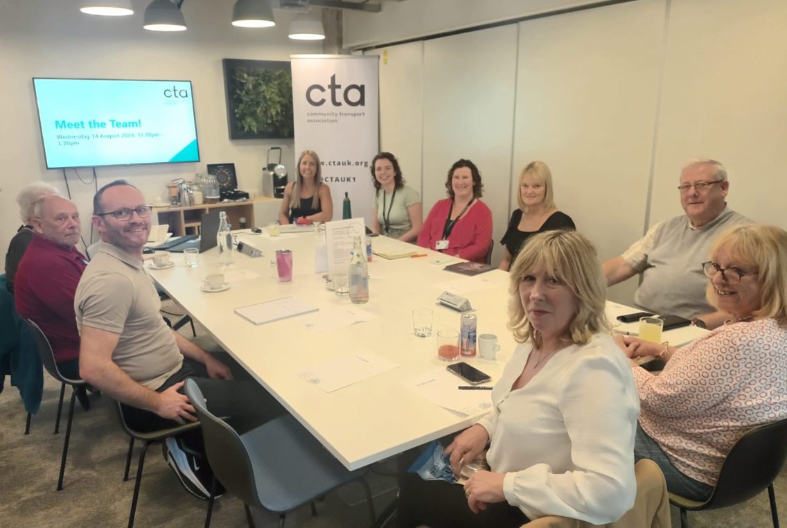 group of people sat around a conference table with a cta banner and screen in the background 