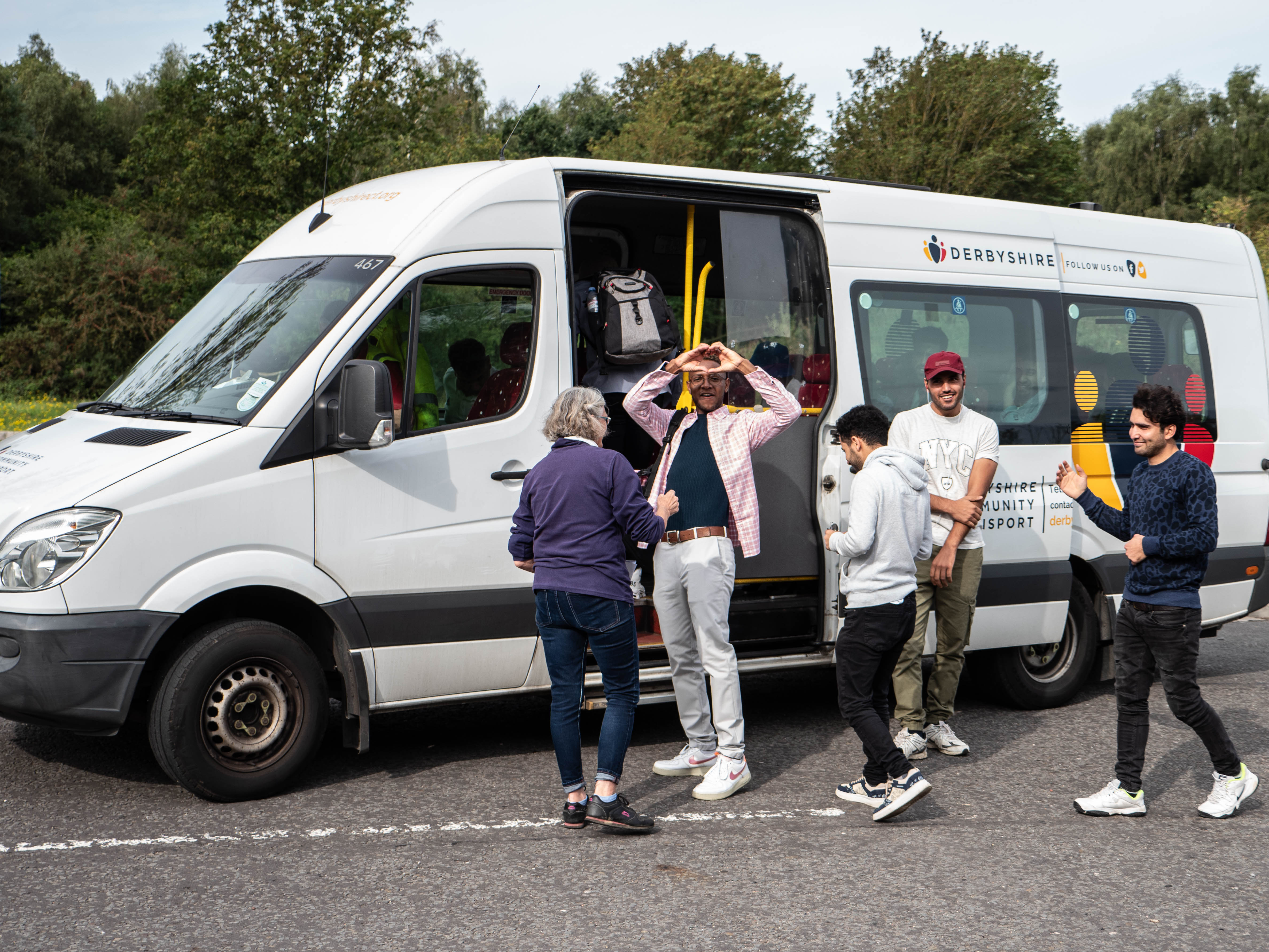 group of young people boarding a minibus. One young man is making a heart shape with his hands. 