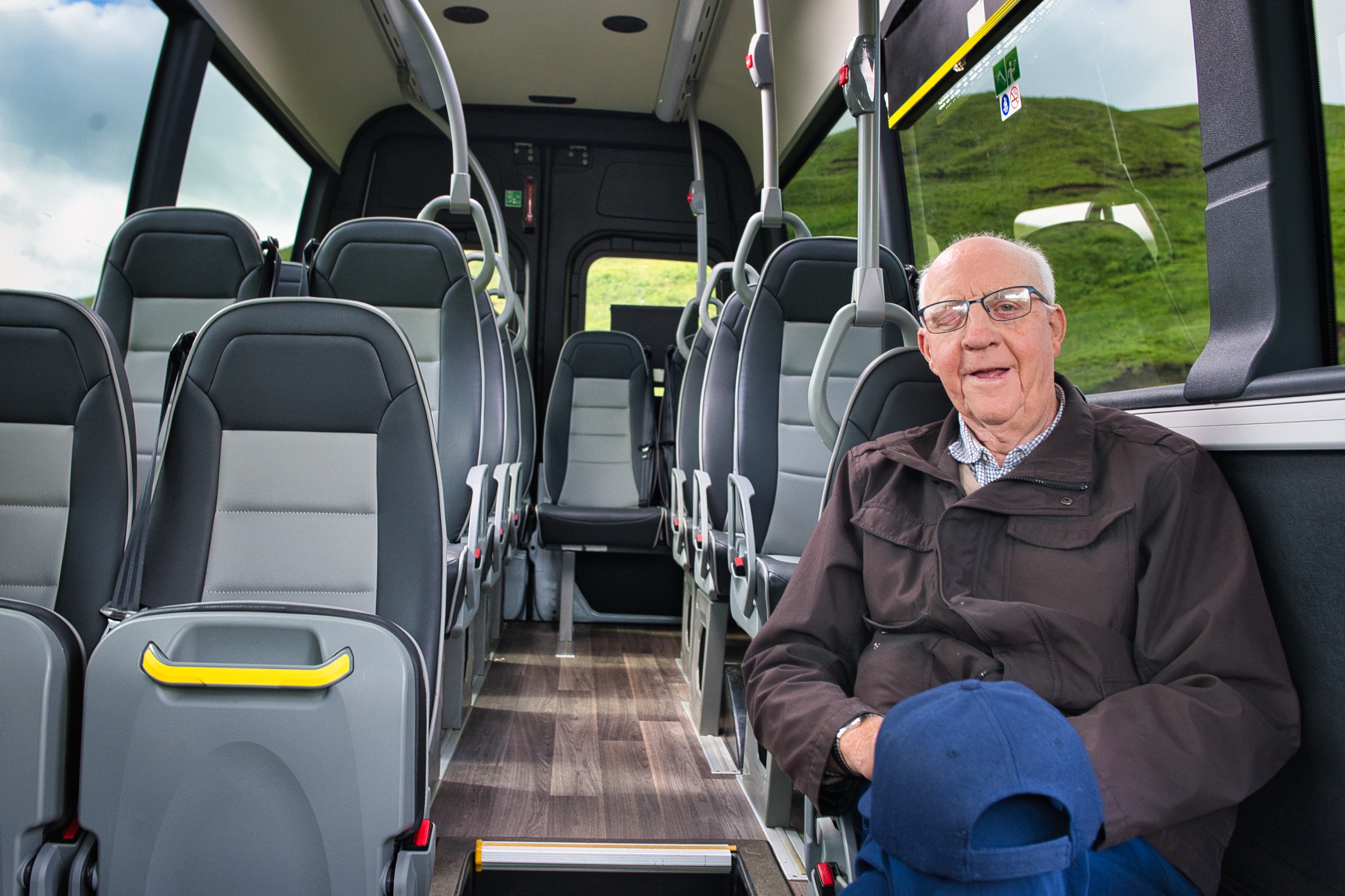 older man with glasses, wearing a dark jacket sitting on an empty minibus 