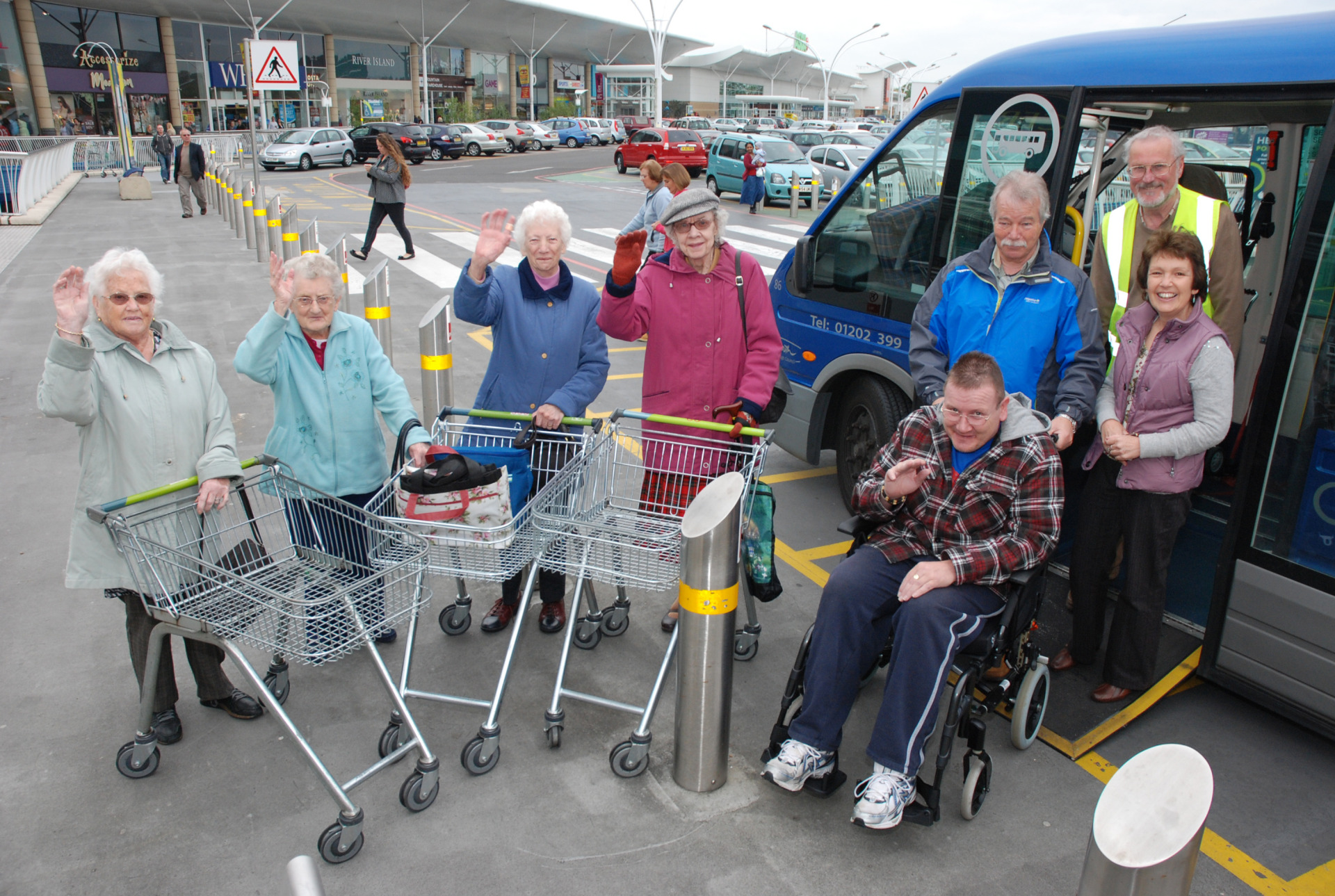 photo of a group of passengers outside a supermarket, with shopping trolleys, waving and smiling.