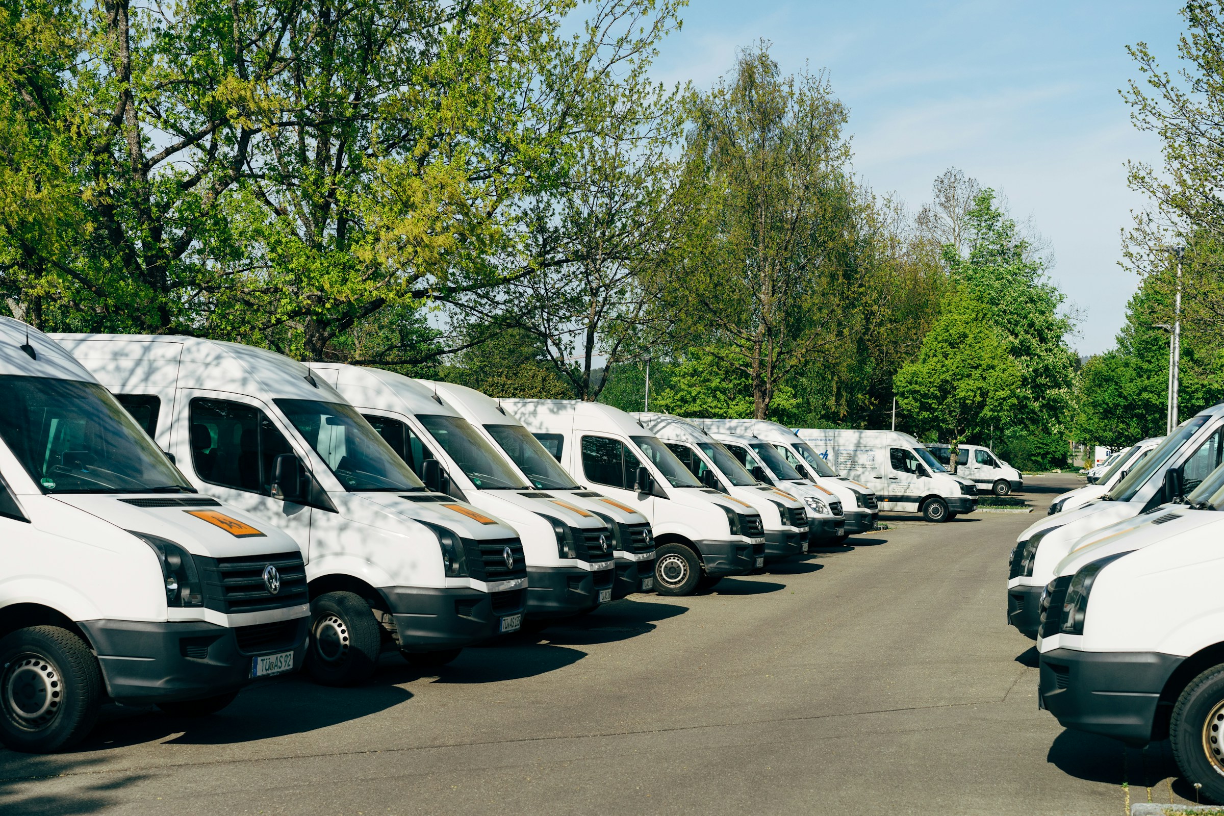 fleet of white mini buses in a car park surrounded by trees and greenery