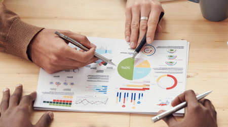 Peoples hands holding pens pointing to graphs on a document