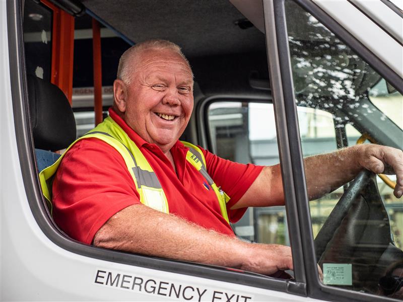 A driver in a high vis vest smiles while sitting at the wheel