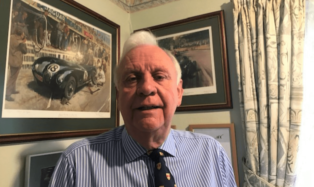 Alan B Jones looking at the camera in a room with photographs of vehicles on the wall behind him