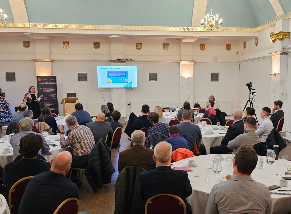 Photo shows CTA Director for Wales, Gemma Lelliott presenting to a room of people sat at conference tables. There is a small screen on the wall and a camera and tripod set up to film. 