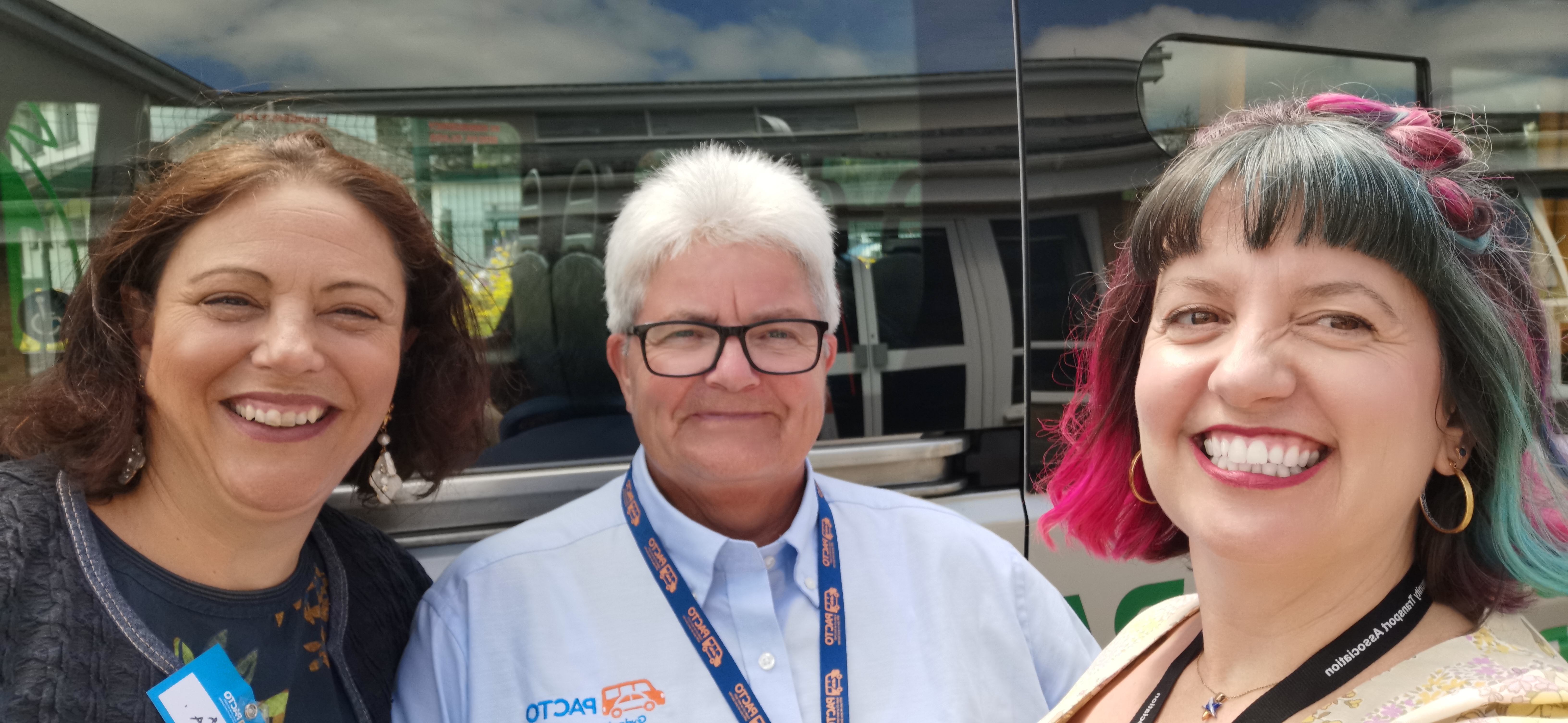 Image of three smiling people standing outside in front of a community transport vehicle