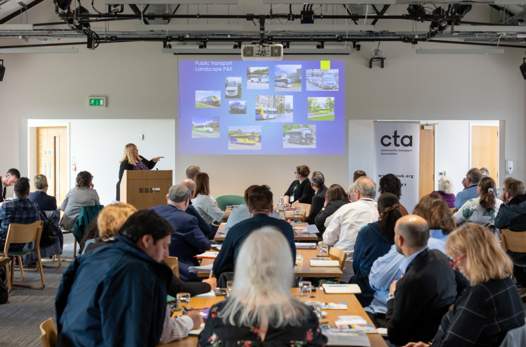 Margaret Roy presenting in front of a blue wall-mounted screen 