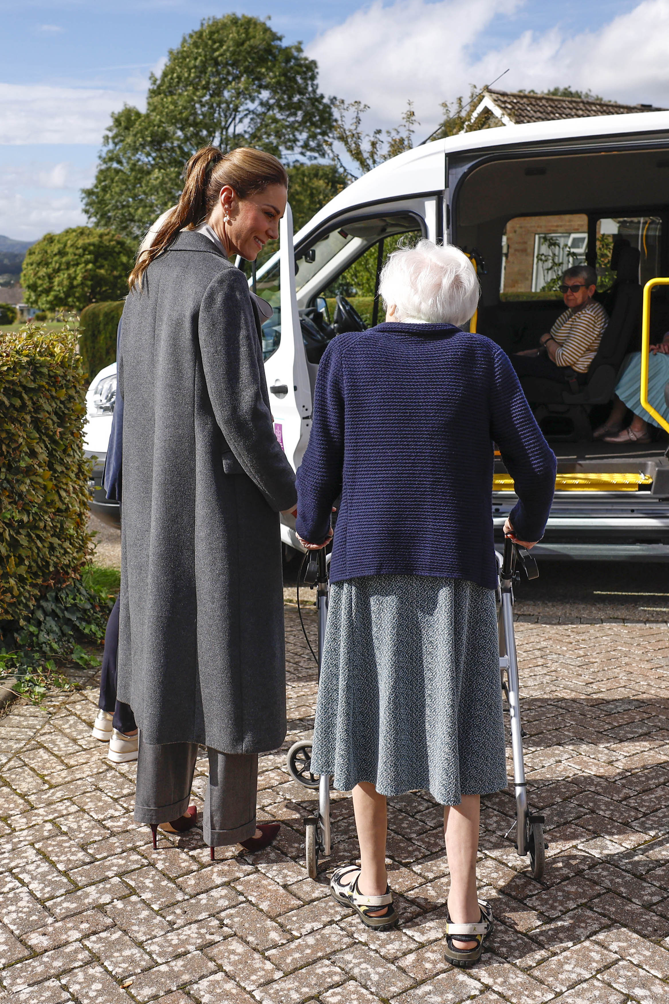 The Princess of Wales walking alongside an older person using a walker to get them to their community transport vehicle