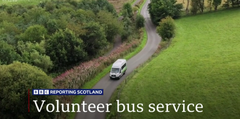 white mini bus driving through the countryside with BBC logo and white text 