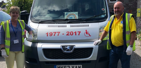 two staff in hi viz jackets standing either side of a minibus 