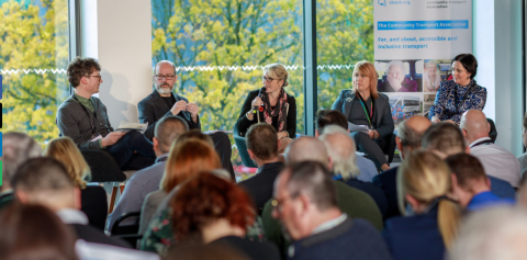 image shows panel talk at conference and people looking on