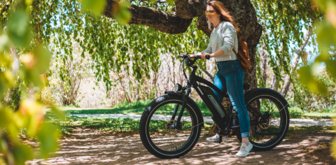 blonde woman on a black bike surrounded by sunlight, green leaves and trees 