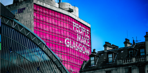 Glasgow building tops with bright pink sign 'people make Glasgow'