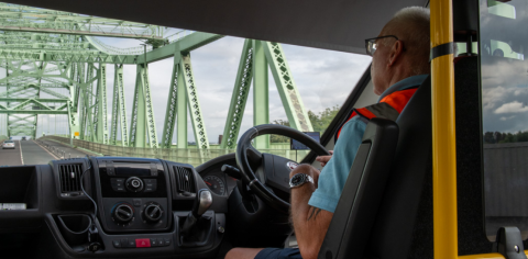 minibus driver in orange hi viz jacket driving over a green bridge 