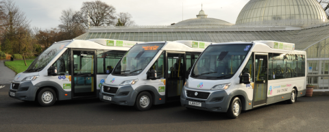 three white and great minibuses lined up with staff stood in front of them smiling