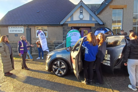 photo showing young people looking around a grey electric car 