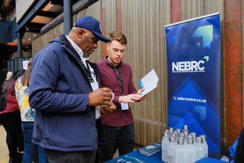 photo shows two men talking and looking at a document in front of a blue NEBR pop up banner. 