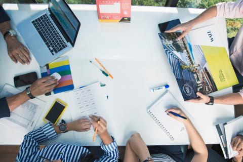 graphic shows a desk with hands, books, phones and laptops from an above view point. 