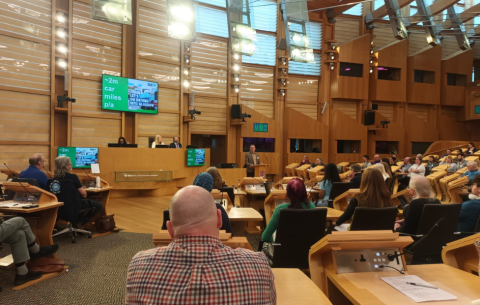 Image of inside the Scottish Parliament building, showing people sitting on their seats watching a presentation
