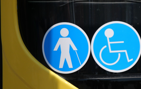 Close-up of blue accessibility symbols on a yellow vehicle window, showing a person with a cane and a wheelchair user.