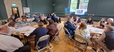 Image of various people meeting in a room with circular tables having a planning session