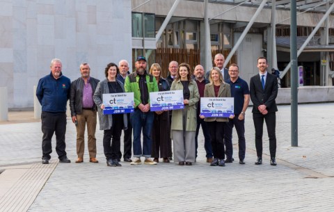 Image of various people standing outside a Parliament building in Scotland holding signs reading "I'm on board for CTWeek".