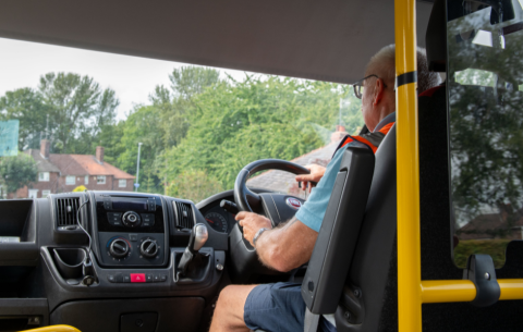 Man driving a vehicle wearing a hi-vis vest showing the inside of the vehicle and some scenery out the window