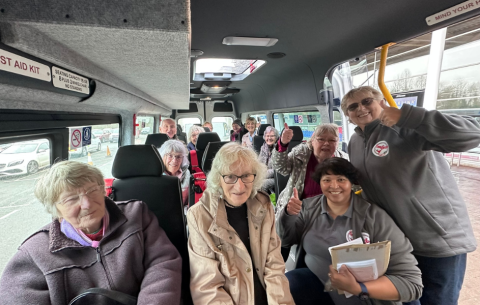 Image of various people sitting in a community transport vehicle smiling