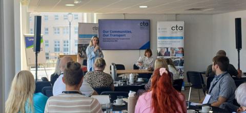 An image of a room filled with people with a presentation board and presenters. There are CTA branded banners in the image.
