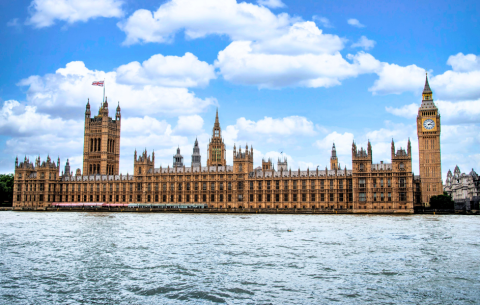 The Houses of Parliament and Big Ben viewed across the River Thames under a bright blue, cloudy sky.