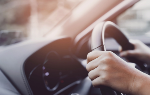 Hands on a steering wheel with light beaming into the window
