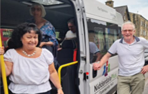 Image of multiple people standing in and around a community transport vehicle out on the street.