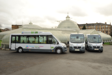 three white minibuses with green and blue livery in front of a white building