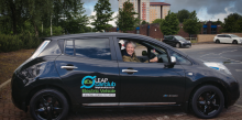 Navy car with logos on the side, blonde lady smiling in drivers seat 