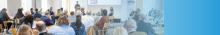 A room filled with people attending a conference and looking at a presentation screen