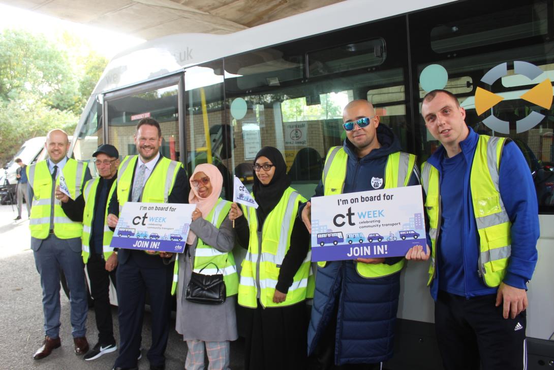 Photo showing a group of people in hi viz vests, holding CTWeek boards, smiling in front of a minibus 