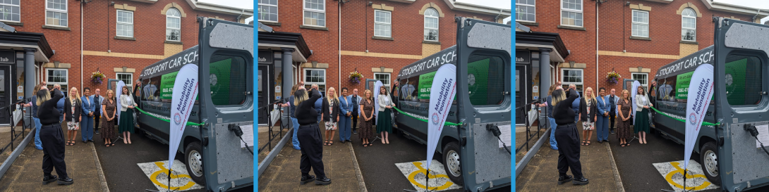 Group of people standing in front of a van with 'Stockport Car Scheme' written on it. The group includes men and women, and they are posing for a photo while a photographer captures the moment. Two 'Motability Foundation' banners are placed next to the van outside a brick building.